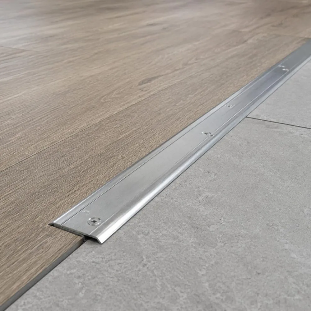 Metal floor transition strip between wood-effect flooring and grey commercial floor surface