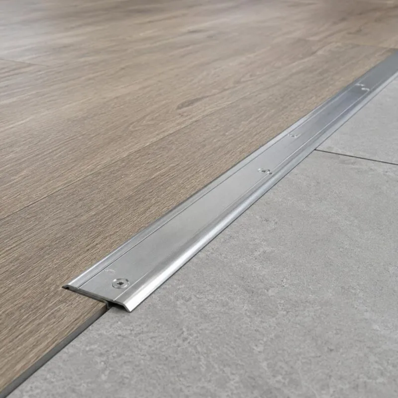 Metal floor transition strip between wood-effect flooring and grey commercial floor surface