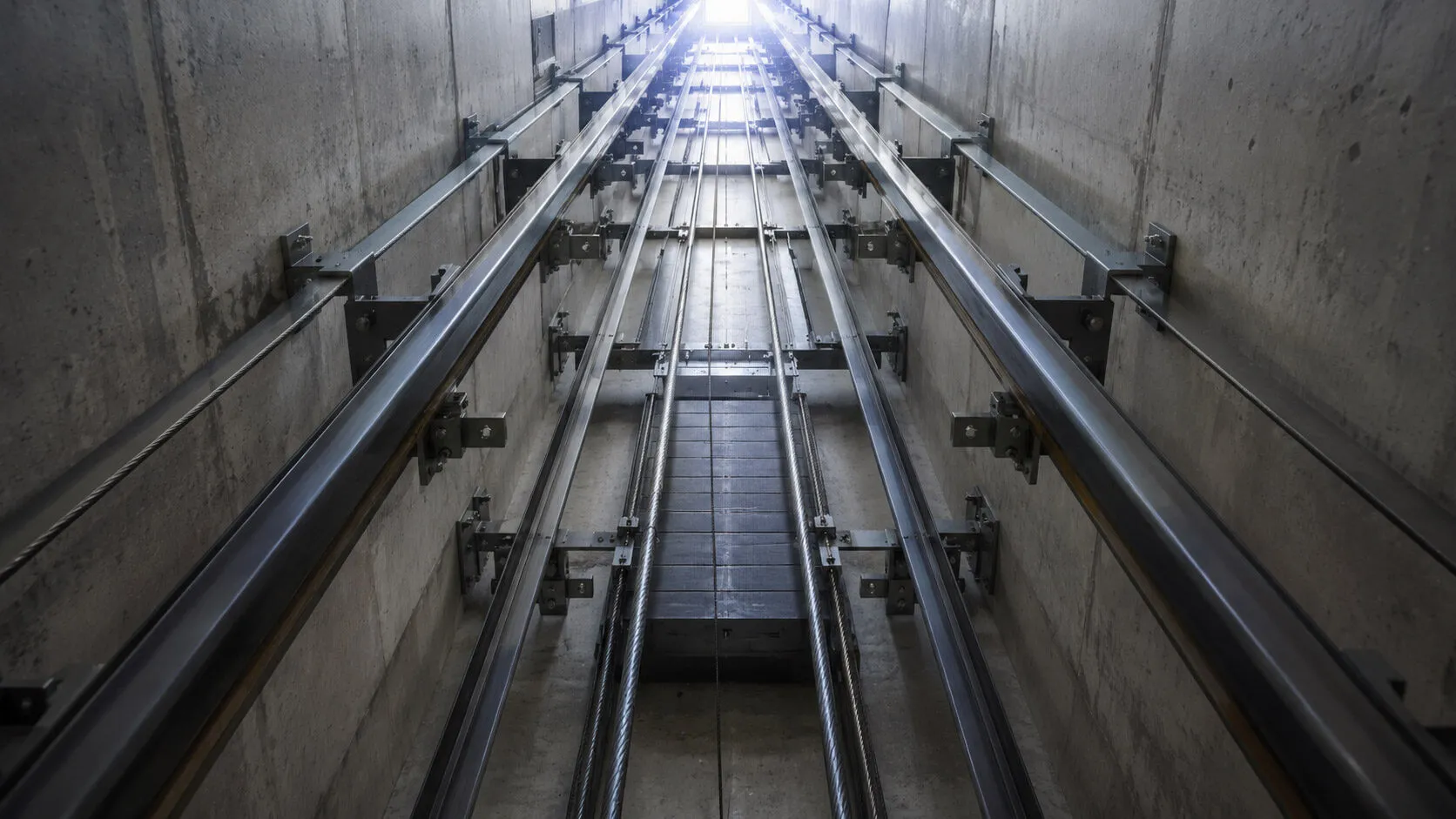 Vertical steel guide rails mounted on shaft walls with brackets at regular intervals